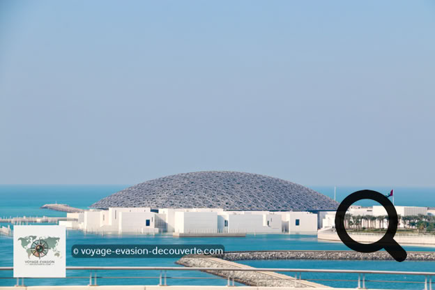 Dès l'arrivée sur l'île de Saadiyat, le bâtiment impressionne par son architecture spectaculaire. Imaginé par l'architecte français Jean Nouvel, le musée ressemble à une cité blanche posée sur l'eau, surmontée d'un immense dôme argenté de 180 mètres de diamètre.